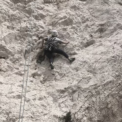 Elisabeth Saehr climbing a pale limestone rock face with a rope and helmet.