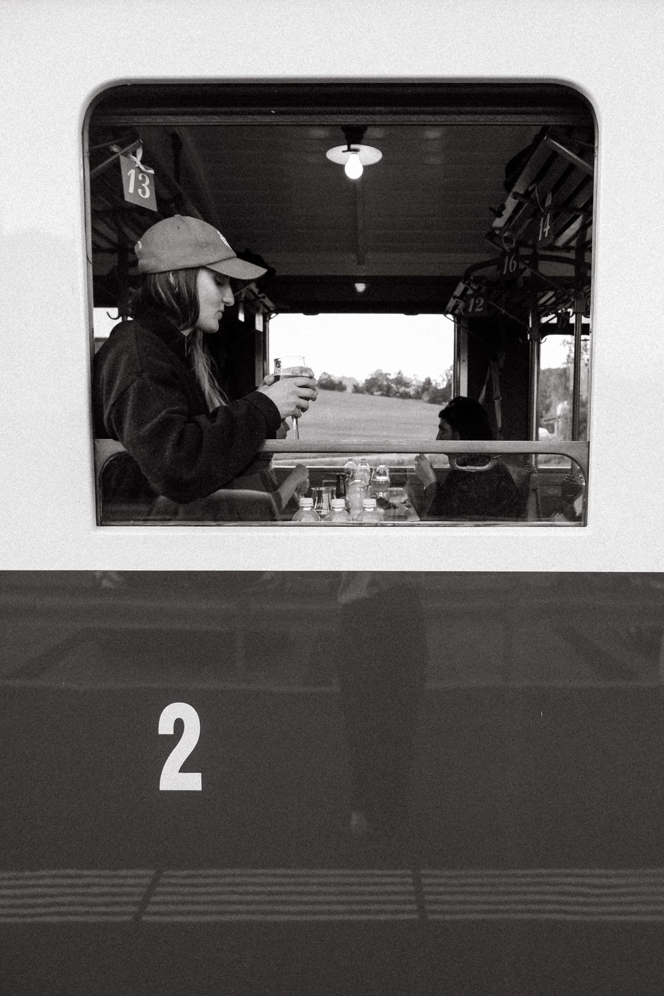 Black and white photo of Elisabeth Saehr in a vintage train carriage, raising a glass by the window.